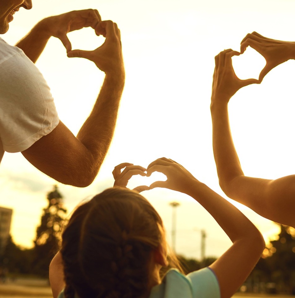 Family of three making heart hands into the sky during sunset
