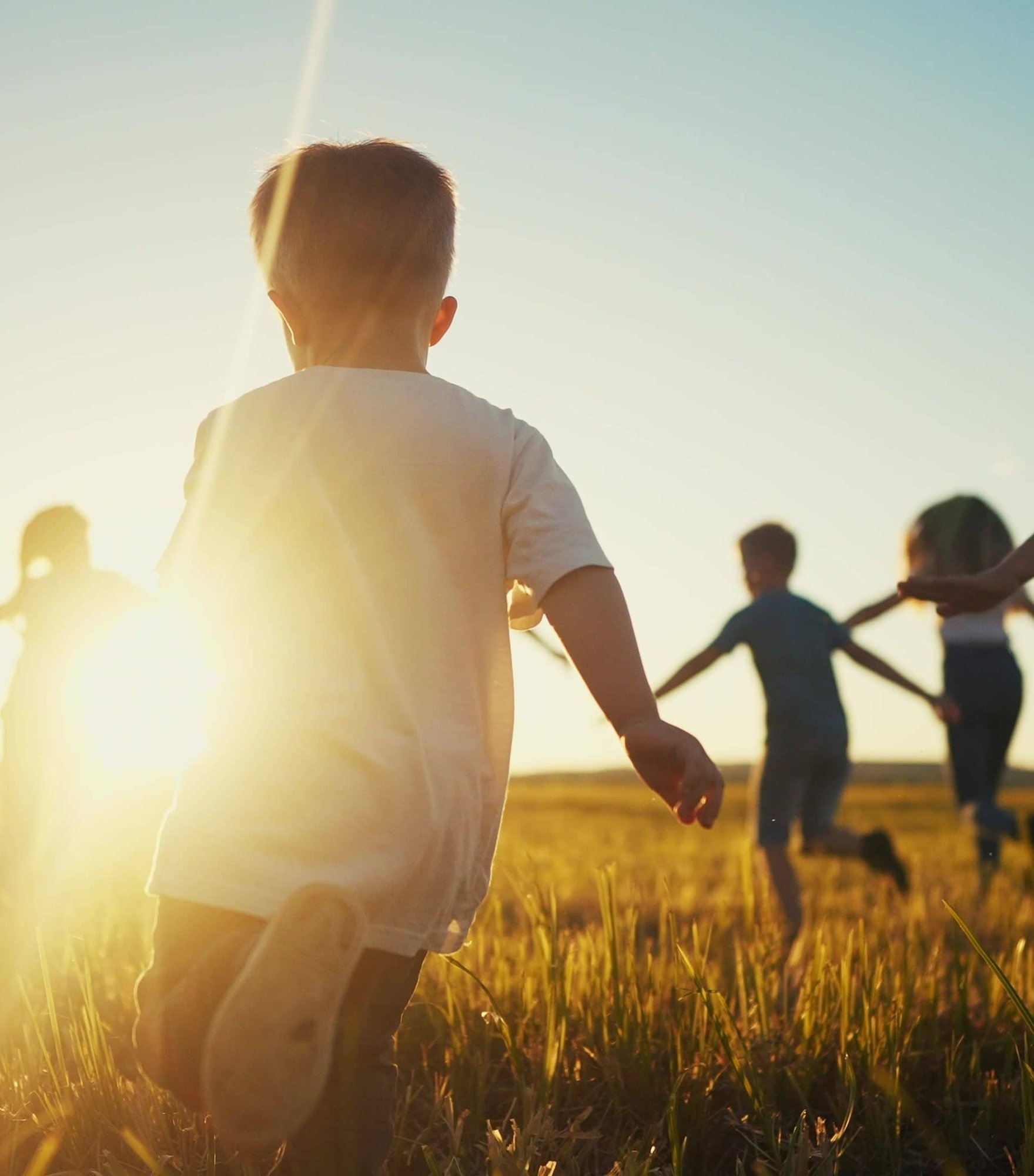 Group of kids running together in an open field during sunset